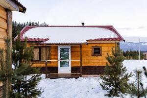 In a picturesque winter scene, a small wooden house featuring a bright red roof is beautifully covered in a layer of soft, white snow, creating a cozy atmosphere and delightful view photo