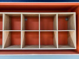 On a vibrant red wall, there is a wellcrafted wooden shelf that features dividers designed to organize items neatly and efficiently, enhancing the aesthetic appeal of the space photo