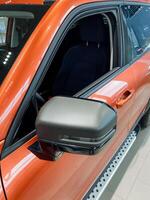 Here is a detailed closeup photograph of a vibrant orange car featuring a sleek black side mirror, showcasing its stylish design and distinctive color that stands out among vehicles photo