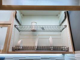 Inside the kitchen, there is a drawer featuring a wire rack that is filled with various plates and cups, providing essential storage and organization for kitchenware and dining items photo