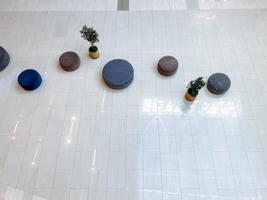 In a beautifully designed space, a group of comfortable ottomans and vibrant potted plants are arranged strategically on a stylish white tiled floor, creating an inviting atmosphere photo