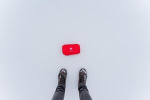 A person is standing in the cold snow next to a bright red box that contrasts with the white winter landscape around them, surrounded by freezing temperatures and precipitation photo