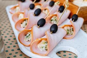 A clean white plate is the perfect backdrop for delightful ham rolls and elegantly presented olives on skewers, creating an appetizing and visually appealing dining experience photo