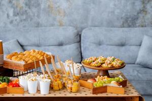 There is a table displaying a wide variety of delicious food items set in front of a cozy couch, creating an inviting atmosphere for enjoyment and dining with friends or family photo