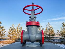 A large, striking metallic valve featuring a vibrant red steering wheel stands out prominently against the surrounding landscape, creating a truly remarkable and eyecatching visual for all photo