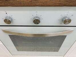 This elegantly designed white oven features shiny silver knobs and a stylish glass door, making it a perfect addition to any modern kitchen space with functionality and aesthetic appeal photo