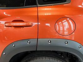 A closeup of an orange car highlights its side gas cap, showcasing a design that effectively combines functionality with aesthetics and includes various automotive features photo