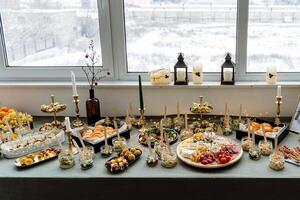 A beautifully arranged table topped with an assortment of plates filled with delicious food and elegantly styled candles sitting in front of a large window providing natural light photo