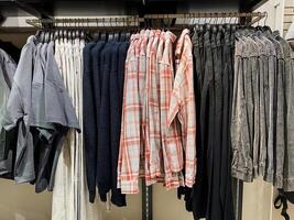 A collection of various clothes is currently displayed and hanging neatly on a rack in a retail store, showcasing different styles and options for potential customers to browse and purchase photo