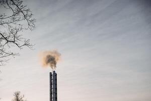 Smoke is gently rising from a chimney, creating a stark contrast against the backdrop of a cloudy sky, adding an atmospheric touch to the natural landscape surrounding it photo
