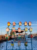 A vibrant and visually striking display of exquisitely crafted, colorful bird houses is set against a picturesque, snowy landscape, collectively creating a lovely and charming winter scene photo