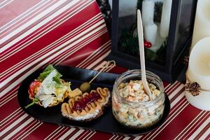 On a table, there is a tray filled with an assortment of food, alongside a jar of fresh salad and a spoon placed conveniently for serving or eating purposes. This setup is quite inviting photo