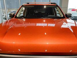 This image features a detailed closeup of an eyecatching orange car displayed within a modern showroom setting, showcasing its sleek design and vibrant color, drawing attention photo