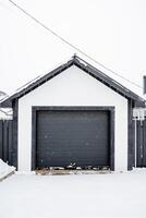 A black and white garage door stands wide open in a heavy layer of snow, showcasing the contrast between the dark door and the bright, white winter landscape surrounding it photo