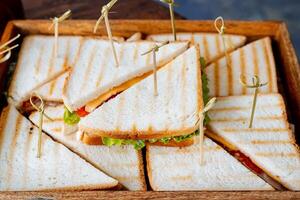 A beautifully crafted wooden box, generously filled with delicious sandwiches that are neatly arranged on toothpicks for easy serving and enjoyment during gatherings or events photo