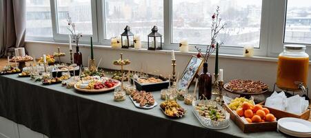 A long table that is abundantly filled with a variety of delicious food and refreshing drinks is placed in front of a large window, allowing sunlight to pour in, enhancing the atmosphere photo