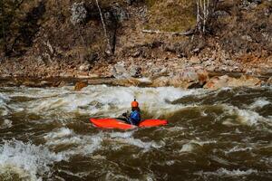 A person skillfully navigates a bright orange kayak on a rushing river, enjoying the thrilling adventure and stunning natural beauty, making the experience unforgettable photo