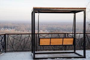 A beautiful wooden swing is positioned on a spacious balcony that provides a stunning view overlooking a lush forest, creating a perfect spot for relaxation and reflection photo