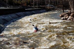 A person is energetically paddling a kayak through the flowing waters of a river, surrounded by the beautiful scenery, showcasing the joy of river kayaking and adventure in nature photo