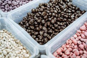 A delightful assortment of various chocolatecovered nuts can be found in convenient plastic containers, perfect for snacking and enjoying as a treat at any time of the day photo