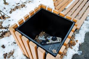 A charming wooden trash can is next to a rustic bench, both covered in a soft layer of white snow, creating an inviting winter wonderland perfect for relaxation and tranquility photo