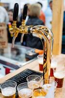 A shiny beer tap pours refreshing golden beer into cups on a polished wooden counter, creating a vibrant atmosphere for patrons to enjoy drinks with friends and fellow guests photo