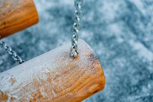 A beautiful wooden swing, complete with chains, is completely covered in a soft layer of white snow, creating a picturesque winter scene that invites playfulness and joy photo