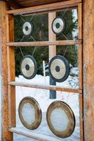 Three gongs made of metal and beautifully crafted are hanging gracefully on a sturdy wooden shelf that is situated in the cold, soft snow, creating a picturesque winter scene photo