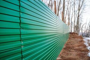 A vibrant green metal fence encloses a winding dirt path that runs through a tranquil wooded area, creating a scenic route for those who enjoy nature walks and exploration photo