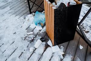 A trash can is placed on a wooden deck that is completely blanketed in a thick layer of fresh, glistening snow, creating a truly picturesque winter scene made up of contrasting elements photo
