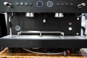 A sleek and modern black coffee machine is elegantly positioned on a rustic wooden table, creating an appealing contrast between the dark appliance and the natural wood grain surface photo