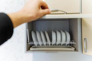 A person is reaching into a wellorganized kitchen cabinet to carefully grab a plate that is stacked neatly on the shelves located inside this functional and efficient space photo