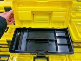 A person confidently grips a bright yellow toolbox, which is wide open, clearly displaying all its contents, indicating a strong readiness to actively use the tools that are inside the box photo