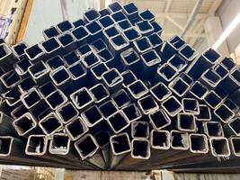 A significant number of squareshaped metal pipes are neatly arranged and stacked one on top of another, creating a tall structure or pile that showcases their uniform shape and size photo