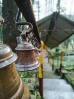 A row of bells hanging from a pole in a forest photo
