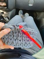 A person is delicately holding a beautifully crafted crocheted basket while also using a vibrant red crochet hook for their creative project, showcasing their crafting skills photo