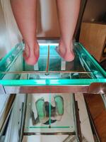 A person is currently having their feet meticulously measured while standing on a transparent glass platform that allows for precise readings and observations to be made photo