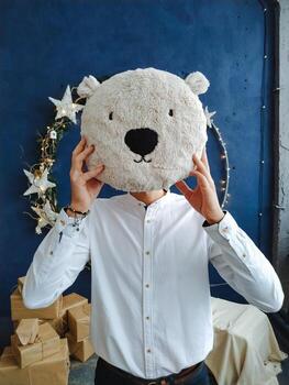 A man is playfully holding a large, fluffy stuffed polar bear head right in front of his face, creating an amusing and entertaining visual effect that is sure to delight onlookers nearby photo