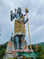 A remarkable large statue of a deity triumphantly holding a trident stands majestically, surrounded by the sky and clouds, surrounded by lush greenery, showcasing stunning art photo
