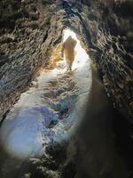 A solitary individual meticulously maneuvers through a dimly lit cave, wielding a powerful light, taking great care to find a secure path as they undertake this demanding expedition photo