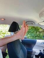 A person is comfortably seated in a car, fully relaxing with their feet propped up on the headrest, taking pleasure in their ride while enjoying the scenic view outside through the window photo