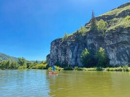 A joyful person is happily floating on a tranquil lake in a bright red kayak, surrounded by stunning natures beauty, fully embracing the peaceful outdoor adventures that life has to offer photo