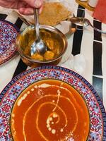 A person is carefully dipping a spoon into a bowl filled with delicious, steaming hot soup, enjoying the comforting aroma that wafts up from the dish, ready to savor each spoonful photo