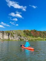 A person is paddling a bright red kayak across a calm and serene lake, completely immersed in the stunning scenery surrounding them and thoroughly enjoying this recreational water activity photo