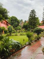 In a beautiful, lush green garden filled with vibrant foliage, there stands a striking red building prominently in the background, creating a stunning visual contrast amid nature photo