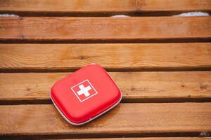 A Compact Red First Aid Kit is placed on a Wooden Surface, ready for use in various Emergency Situations that may arise during your outdoor activities or daily life routines photo