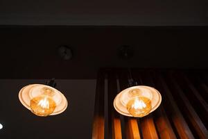 In a cozy, dimly lit room, two inviting bulbs hang from the ceiling, casting a soothing glow that dispels darkness and creates a serene atmosphere for relaxation and enjoyment photo