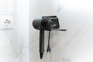 In the bathroom, a hair dryer is conveniently hanging on the wall, providing easy access for users who want to style their hair quickly and efficiently while getting ready photo