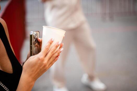 A woman expertly balances a steaming cup of coffee in one hand while using a smartphone in the other, demonstrating her impressive multitasking skills in a techdriven setting photo