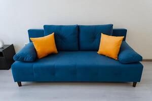The living room feels cozy with a chic azure couch and vivid orange pillows creating a warm and inviting atmosphere. It exudes comfort and character, making it a delightful space to relax photo